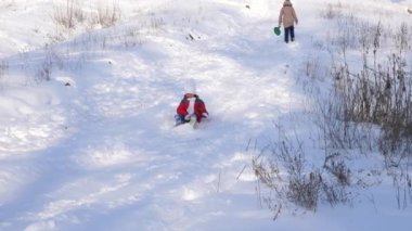 Kırmızı ceketli genç kız kış Park'ta bir yüksek karlı tepeden kızak üzerinde slaytlar. Kız gülüyor ve sevinir.