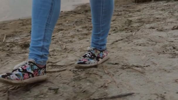 Benen van het meisje gaan op het strand in jeans en sneakers. Close-up — Stockvideo