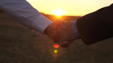 gün batımında el sıkışma. adam mavi gömlek ve ceket ve Beyaz tişörtlü adam güzel bir gün batımı ışınlarının batımında el sıkışın. yakın çekim.