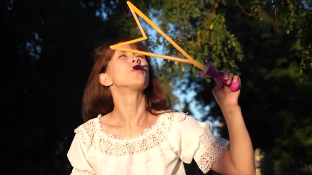 Menina deixa grandes bolhas no parque da cidade e sorrindo. Movimento lento — Vídeo de Stock