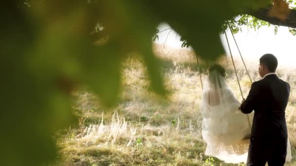 mariée en robe blanche et marié swing sur swing dans le parc en été. balançoire sur une branche de chêne .