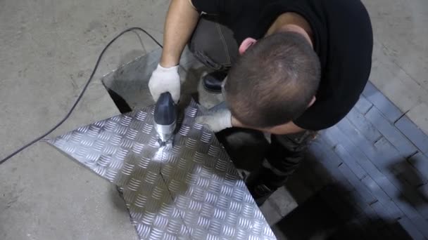 Trabajador en gafas protectoras sierra una lámina de hierro brillante con una sierra de plantilla eléctrica en guantes protectores blancos. vista desde arriba — Vídeos de Stock