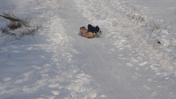 Ragazza rotola su slitta da un alto scivolo innevato. ragazza gioca in inverno nel parco. Rallentatore — Video Stock