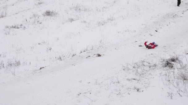 Девушка едет по белым снежным горам и падает теряя кепку. Рождественские каникулы. Зимние игры. Медленное движение — стоковое видео