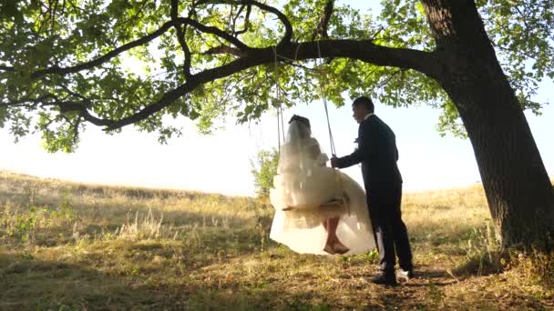 Sposa e sposo cavalcare su altalena nel parco. felice coppia innamorata dondolando sull'altalena nella foresta — Video Stock