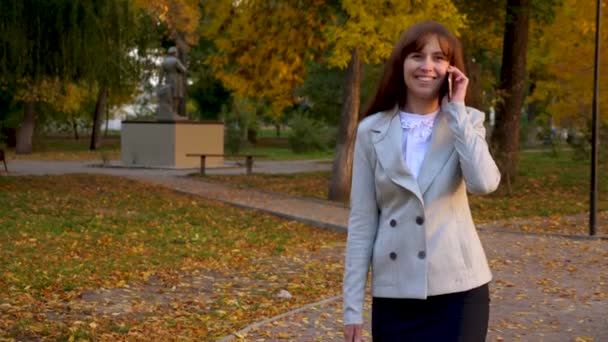 Piękna kobieta rozmawia na smartfonie spacery w parku i uśmiecha się. biznes kobieta nosi czarnej teczki z dokumentami w ręku. — Wideo stockowe