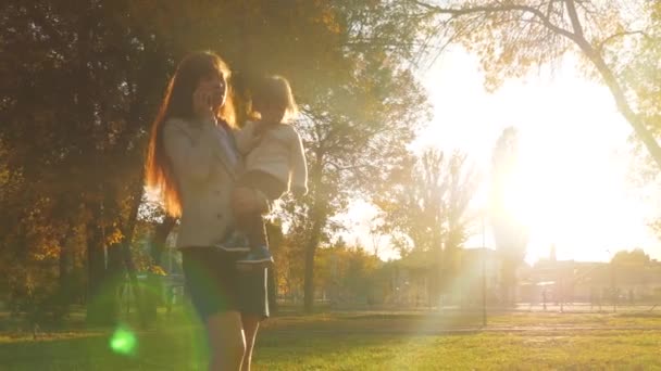 Mère porte l'enfant dans ses bras et parle sur son téléphone portable. promenades en famille le soir dans le parc de la ville . — Video