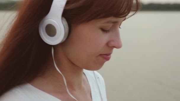 Chica en los auriculares está aprendiendo en la tableta en la orilla del mar y sonriendo. Mujer de compras en línea en la tienda online. Primer plano — Vídeos de Stock
