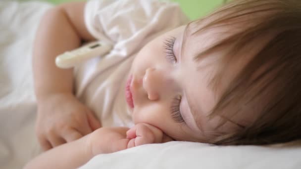 Θερμοκρασία μωρού μετριέται με το θερμόμετρο στο νοσοκομείο ward. το παιδί κοιμάται στο νοσοκομείο ward σε ένα λευκό κρεβάτι. — Αρχείο Βίντεο
