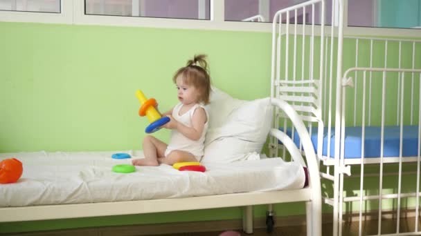 Bebê brinca na cama com pirâmide e anéis coloridos. Brinquedos educativos para crianças pré-escolares e do jardim de infância. Brinquedo para o Kid. criança brinca na enfermaria do hospital na cama . — Vídeo de Stock