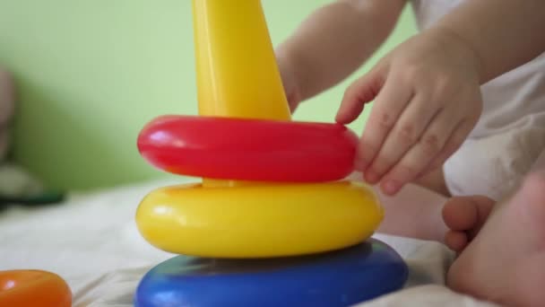 Hands of the child are playing with pyramid and colored rings on bed. close-up. Educational toys for preschool and kindergarten children. Toy for Kid. child plays in room on the bed. — Stock Video