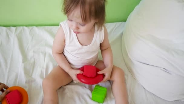 Kind spielt im Zimmer auf weißem Bett mit roten und grünen Würfeln und Ringen. Lernspielzeug für Vorschul- und Kindergartenkinder. Spielzeug für Kinder. Baby und Mama spielen mit buntem Spielzeug auf dem Bett. — Stockvideo