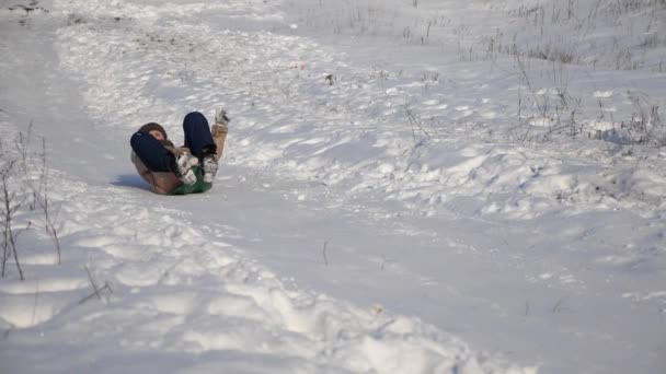Молодая девушка скатывается с холма на санях в снегу. Девушка играет зимой в Рождественском парке. Медленное движение — стоковое видео