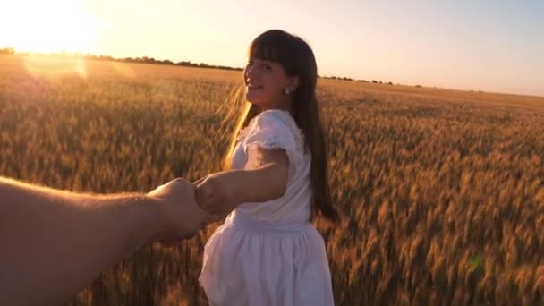 Chica riendo corre por el campo con trigo sosteniendo una mano de hombre en el resplandor del sol dorado. Movimiento lento . — Vídeos de Stock