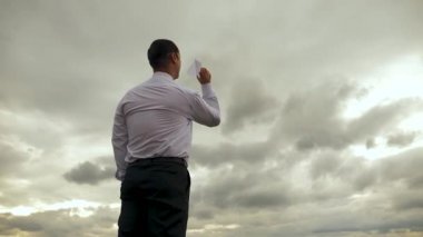 Beyaz gömlekli işadamı kara bulutlar çerçevede uçak uçan kağıt ile oynuyor. Ağır çekim