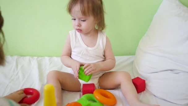 Bebé y mamá jugando con juguetes de colores en la cama. niño juega en la habitación en la cama blanca con cubos y anillos rojos y verdes . — Vídeos de Stock