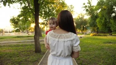küçük kızı annesinin elinde mutlu aile yaz parkta yürüyor. ağır çekim