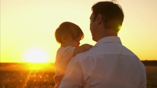 Papá camina con un niño pequeño en sus brazos en el parque nocturno en otoño al atardecer. Papá e hija pasan un día libre juntos. . — Vídeos de Stock