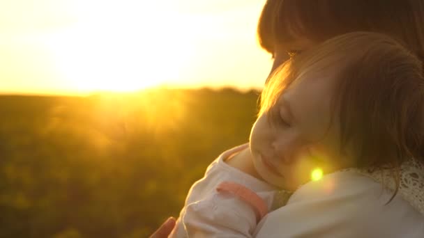 Küçük kız bir günbatımı altın ışınları genç anne kollarında uyuyor. Ağır çekim — Stok video