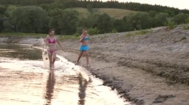 Mayolu genç kızların plaj boyunca yaz ve gülmek çalıştırın. nehir kıyısında mutlu çocuklar yalınayak koşmak