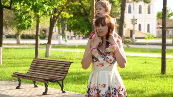 Feliz mãe carrega pequena filha em seus ombros, andar no parque com uma criança — Vídeo de Stock