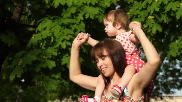 Anne küçük kızı onun omuzlarında taşıyan, bir çocukla parkta yürümek — Stok video