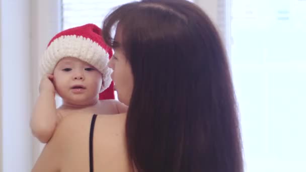 Dziecko w Santaklaus kapelusz z mama w jej ramiona. małe dziecko Santa Claus gry z jego mama na święta Bożego Narodzenia. Szczęśliwa rodzina świętuje Boże Narodzenie. koncepcja rodzinne wakacje. — Wideo stockowe