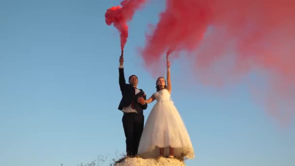 Novia feliz y novio agitando humo de color rojo contra el cielo azul . — Vídeos de Stock