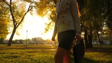 kadın onun elinde çanta taşır ve parlak güneş ışınlarının parkında kaldırım boyunca yürür. yakın çekim.