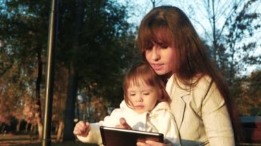 Anne ve çocuk parkta bir bankta oturup tablet.