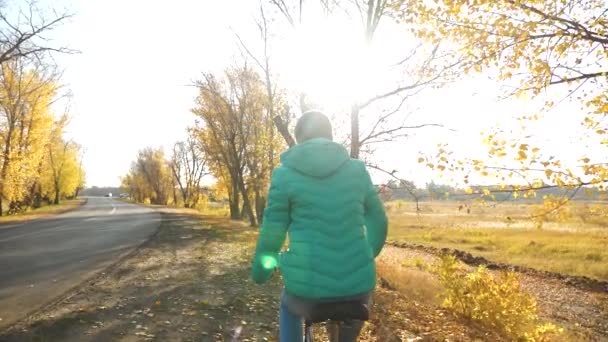 Jovem menina de jaqueta rosa andar de bicicleta iluminada por raios de sol no parque de outono. Movimento lento . — Vídeo de Stock