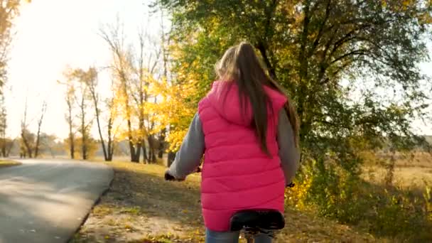mladá dívka na koni kolo na silnici v podzimním parku a usmívá se. Zpomalený pohyb.