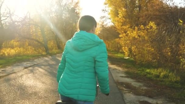 Flicka rider cykel på en asfalterad väg i höst park på bakgrunden av gula träd — Stockvideo