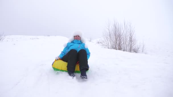 Fille heureuse glisse à travers la neige sur traîneau, belle jeune femme glisse vers le bas glisser dans la neige sur un tube à neige gonflable et agite sa main. fille jouant dans le parc pour les vacances de Noël en hiver — Video