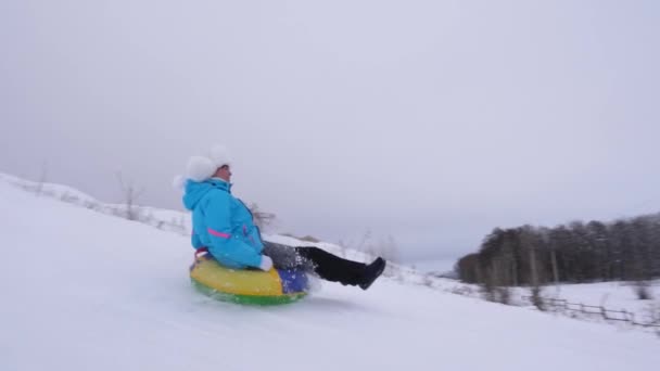 Szczęśliwa młoda dziewczyna slajdy w dół slajdu w śniegu na tube nadmuchiwane śniegu i fale jej rękę. Dziewczyna w parku na święta Bożego Narodzenia w zimie. Zwolnionym tempie. — Wideo stockowe
