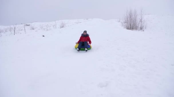 Happy young girl slides from high snow slide an inflatable snow tube. children play in winter in park in the Christmas holidays. rolls down hill in sleigh. — Stock Video