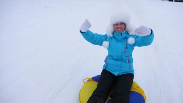 Hermosa mujer joven se desliza deslizar en la nieve en un tubo de nieve inflable y olas mano. Chica feliz se desliza a través de la nieve en el trineo. chica jugando en el parque para las vacaciones de Navidad en invierno — Vídeos de Stock