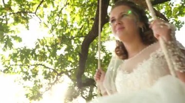 Beyaz elbiseli bir meşe dalı Park'ta salıncak üzerinde sallanan mutlu gelin. yakın çekim