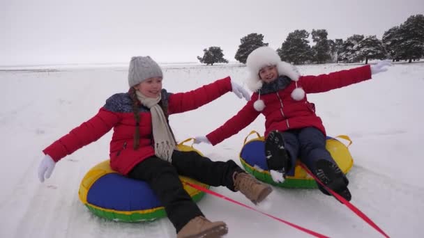 Kinder fahren im Winter auf einer aufblasbaren Schneeröhre durch den Schnee. Mädchen entspannen sich im Winterpark für die Weihnachtsfeiertage. Zeitlupe — Stockvideo