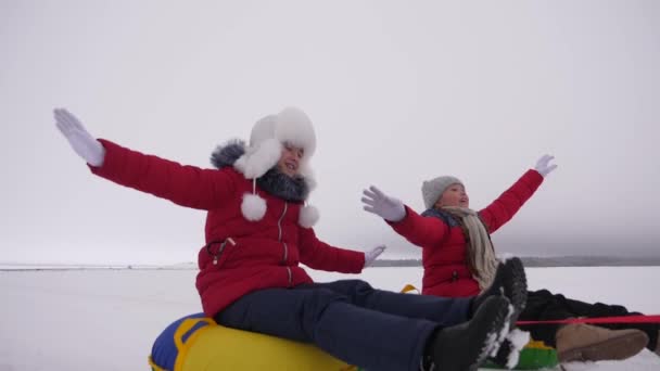 Crianças em jaquetas vermelhas passeio através da neve no inverno em um tubo de neve inflável e jogar super-heróis. meninas felizes relaxando no parque de inverno para férias de Natal. Movimento lento — Vídeo de Stock