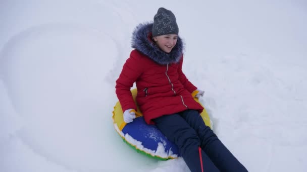 Adolescente chica juega en un parque de invierno en las vacaciones de Navidad. chica se desliza en invierno en la nieve de alta colina en trineo y un tubo de nieve inflable. Movimiento lento . — Vídeos de Stock