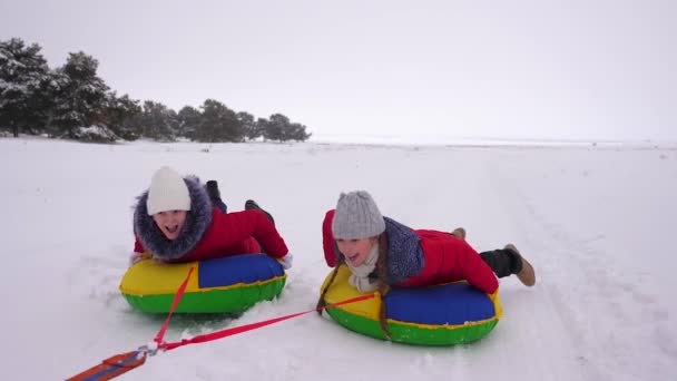 Niños en chaquetas rojas en invierno paseo a través de la nieve en un tubo de nieve inflable y en trineo. deporte niñas relajarse en el parque de invierno para las vacaciones de Navidad. Movimiento lento — Vídeo de stock