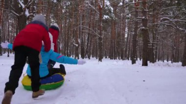 Mutlu çocuk anneleri kızak ve çam ormanı içinde bir şişme kar tüp binmek. mutlu aile anne ve kış park ve orman içinde Noel tatili için oynayan çocuklar. Ağır çekim.