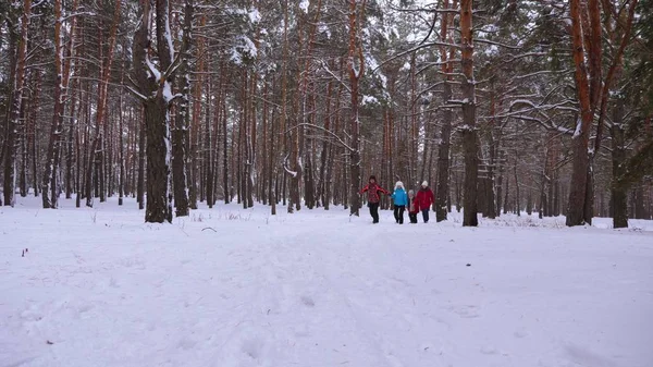 Crianças felizes e mamãe e papai correm com as crianças na floresta de inverno. os pais brincam com crianças em um parque nevado no inverno. família feliz caminha na floresta de Natal. trabalho em equipa — Fotografia de Stock