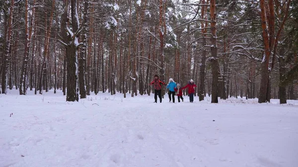 Niños felices y mamá y papá corren con los niños en el bosque de invierno. los padres juegan con los niños en un parque nevado en invierno. familia feliz camina en el bosque de Navidad. Trabajo en equipo —  Fotos de Stock