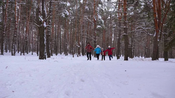 Enfants heureux et maman et papa courent avec les enfants dans la forêt d'hiver. les parents jouent avec les enfants dans un parc enneigé en hiver. joyeuses promenades familiales dans la forêt de Noël. le travail d'équipe — Photo