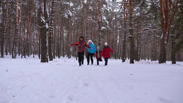 Glückliche Kinder und Mama und Papa laufen mit den Kindern im Winterwald. Eltern spielen im Winter mit Kindern in einem verschneiten Park. glückliche Familienspaziergänge im Weihnachtswald. Teamarbeit — Stockfoto