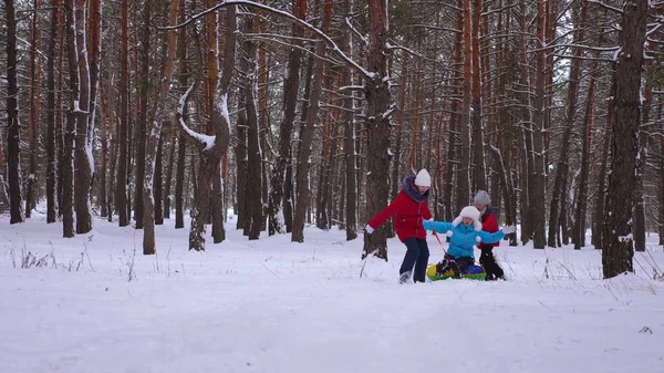 Lustige Kinder fahren mit ihrer Mutter auf Schlitten und einem aufblasbaren Schneeschlauch im Kiefernwald. glückliche Familie Mutti und Kinder spielen im Winter Park und Wald für die Weihnachtsfeiertage. — Stockfoto