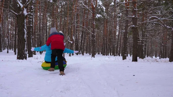 Los niños felices montan a su madre en trineo y un tubo de nieve inflable en el bosque de pinos. familia feliz mamá y los niños jugando en el parque de invierno y el bosque para las vacaciones de Navidad. Movimiento lento . —  Fotos de Stock