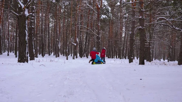 Glückliche Kinder fahren mit ihrer Mutter auf Schlitten und einem aufblasbaren Schneeschlauch im Kiefernwald. glückliche Familie Mutter und Kinder spielen im Winter Park und Wald für die Weihnachtsfeiertage. Zeitlupe. — Stockfoto